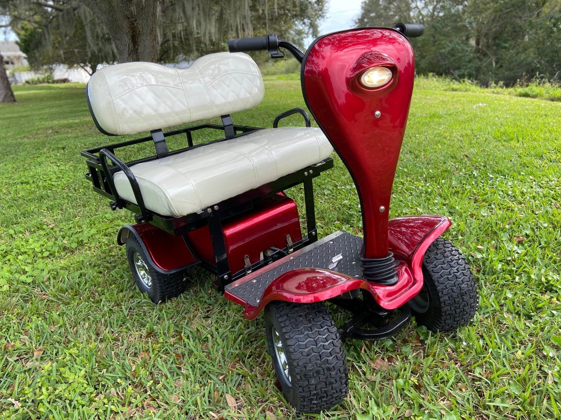 A red golf cart with a white seat is parked in the grass.