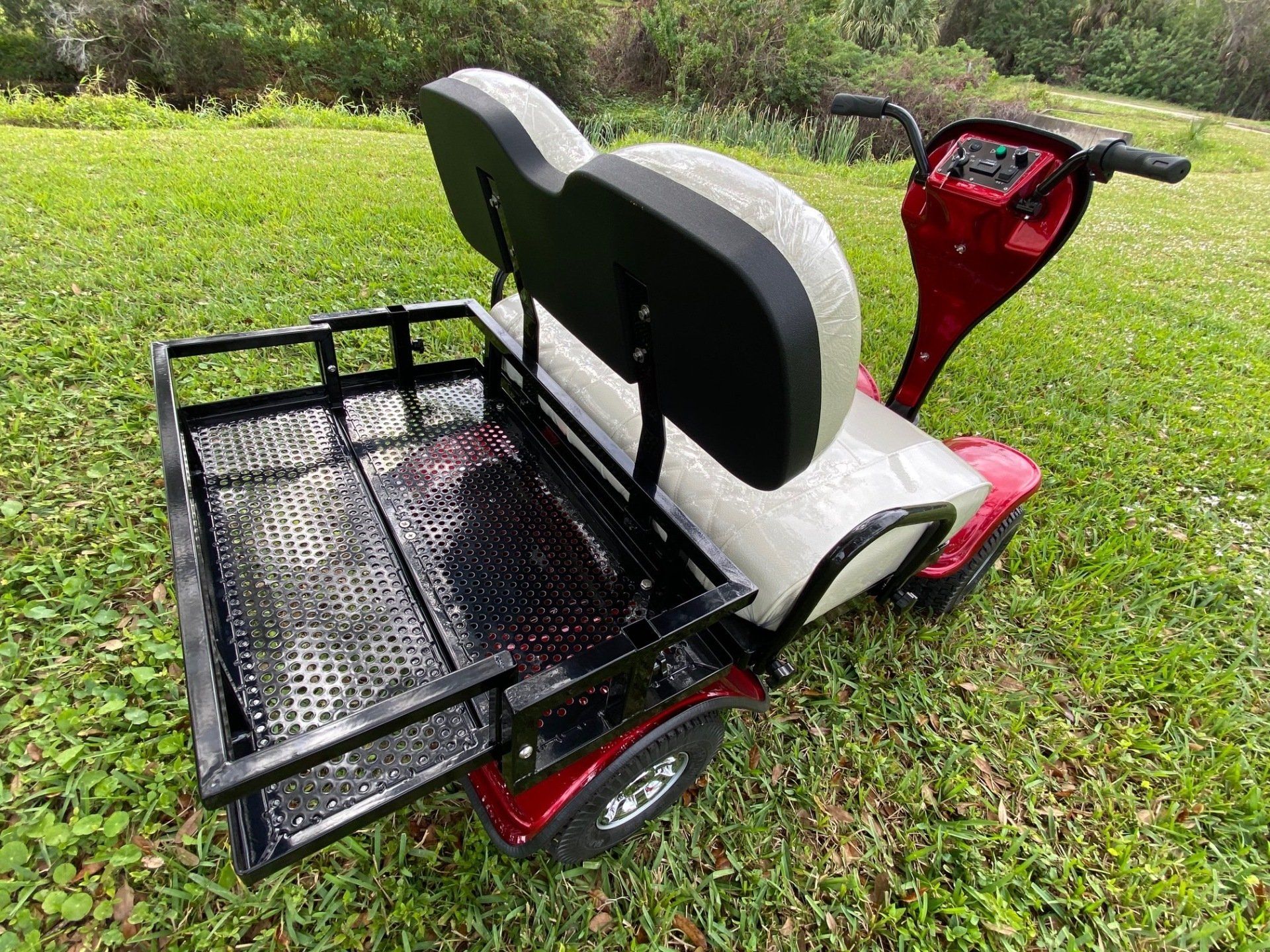 A red golf cart with a basket attached to the back is parked in the grass.
