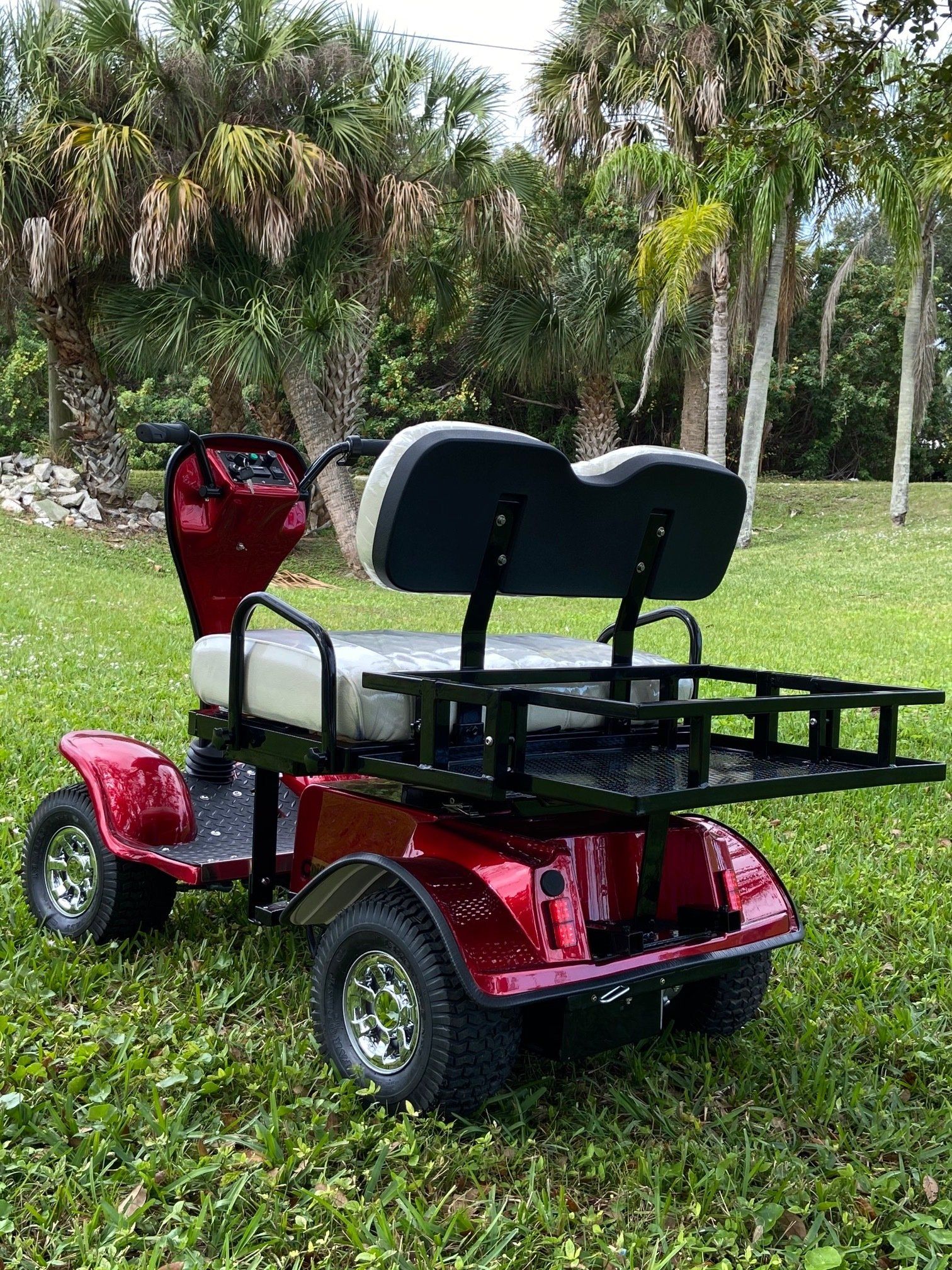 A red golf cart with two seats is parked in the grass.