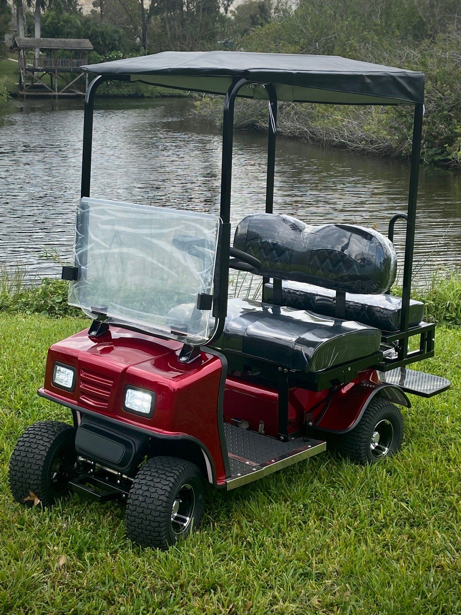 A red golf cart is parked in the grass near a body of water.