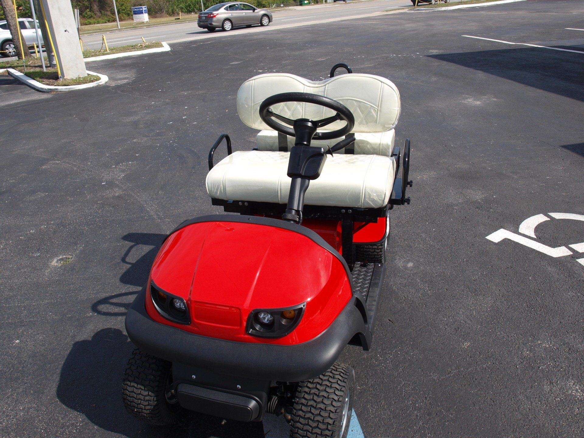A red golf cart is parked in a handicapped parking spot