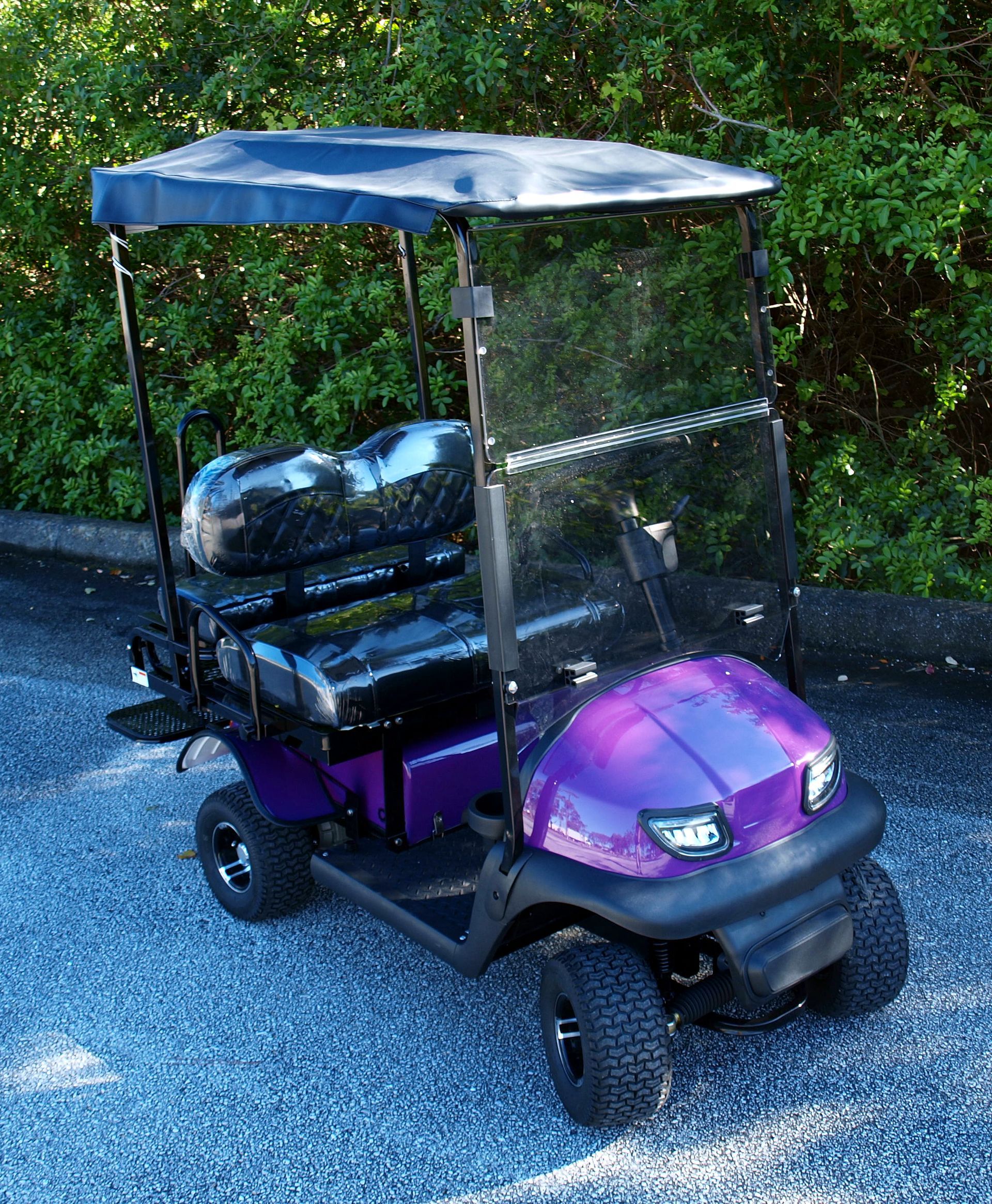 A purple golf cart with a canopy is parked on gravel.