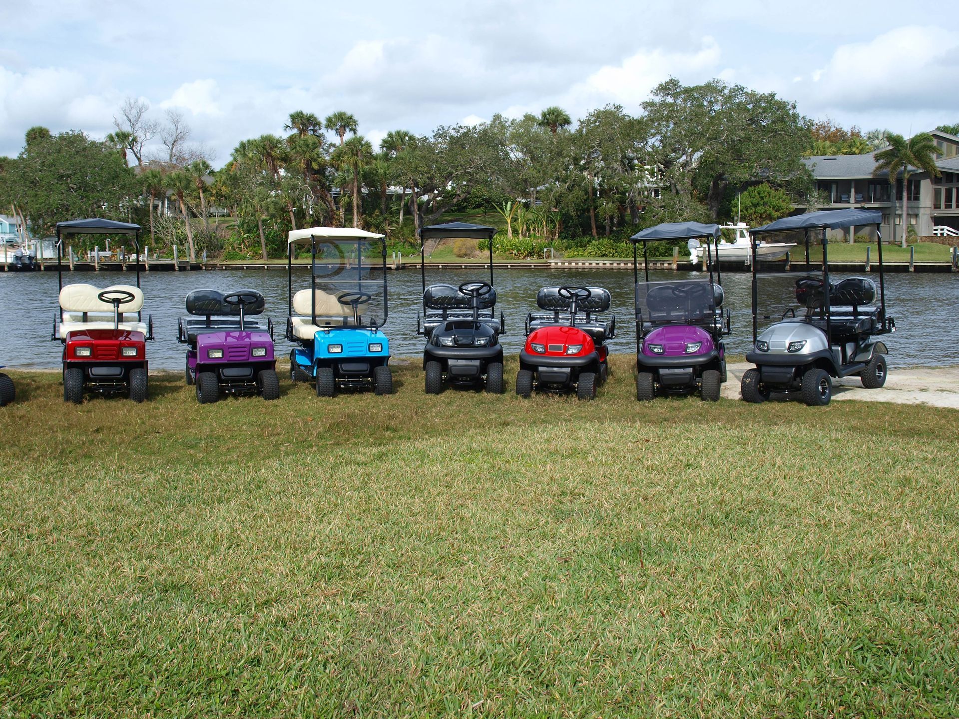A row of golf carts are parked in a grassy field next to a body of water.