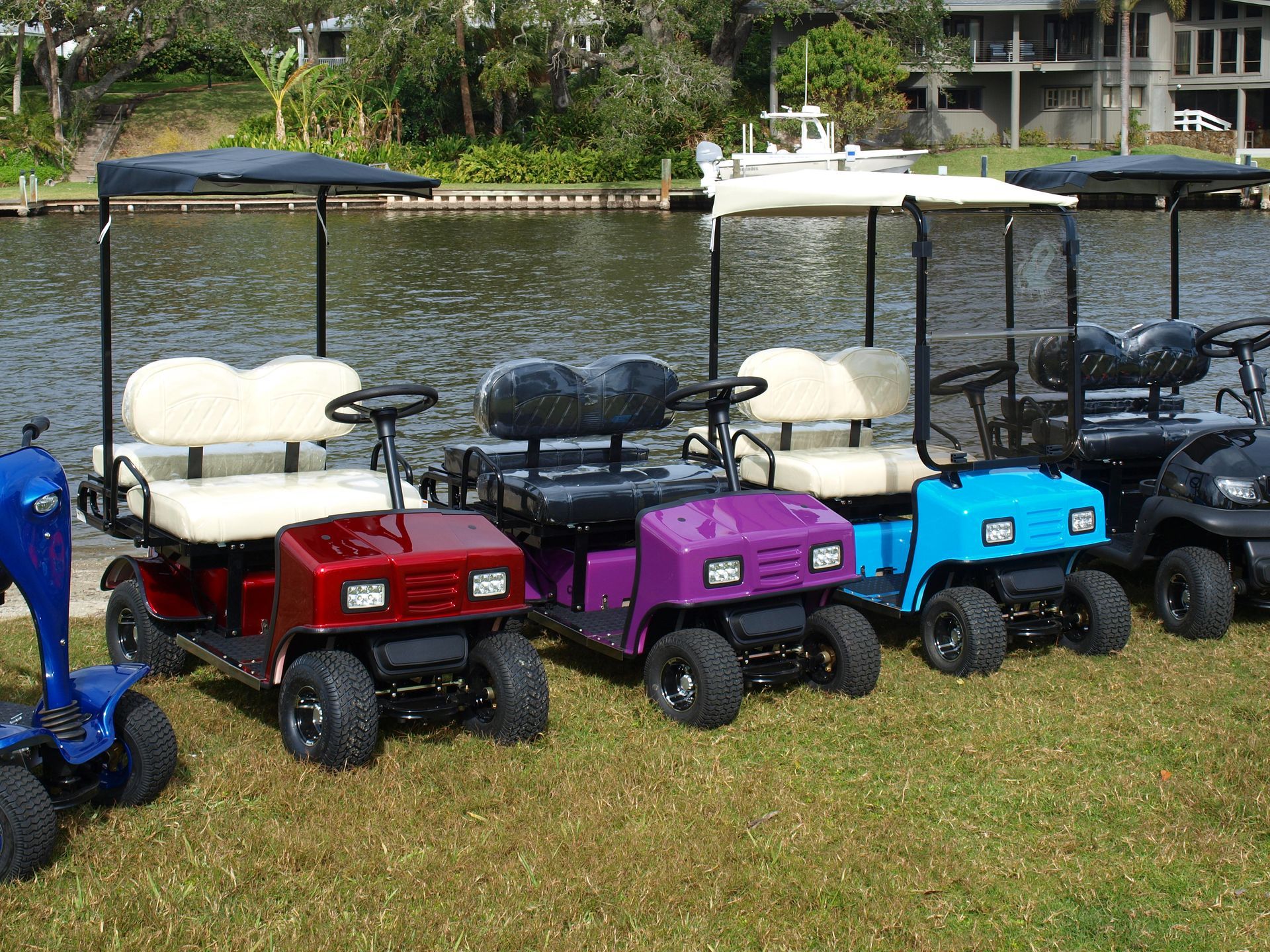 A row of golf carts are parked in a grassy area near a body of water.