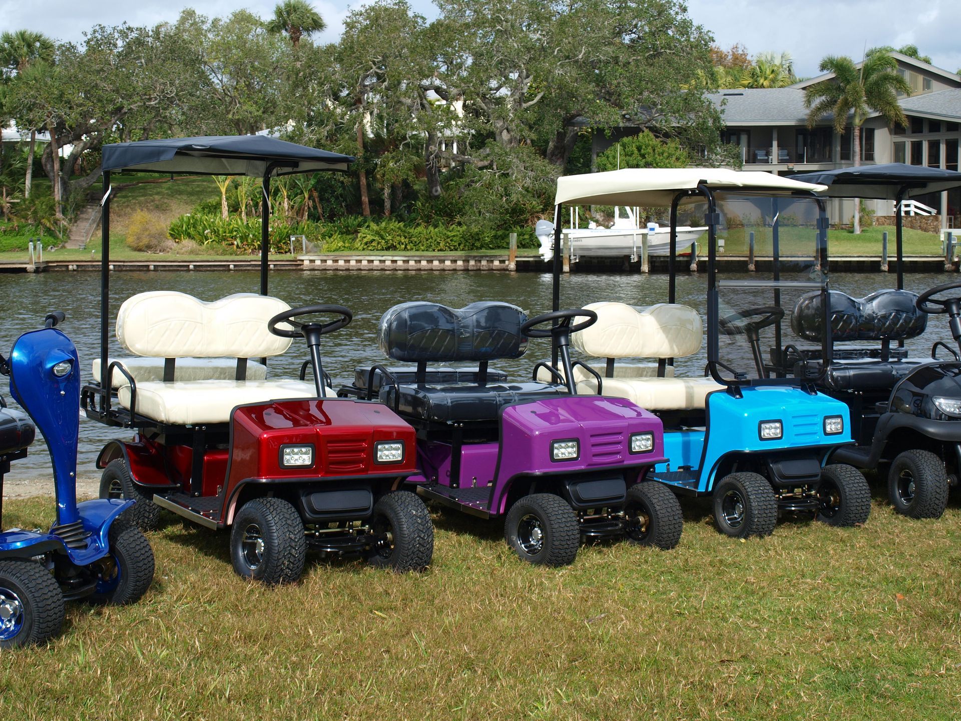 A row of golf carts are parked on the grass near a body of water