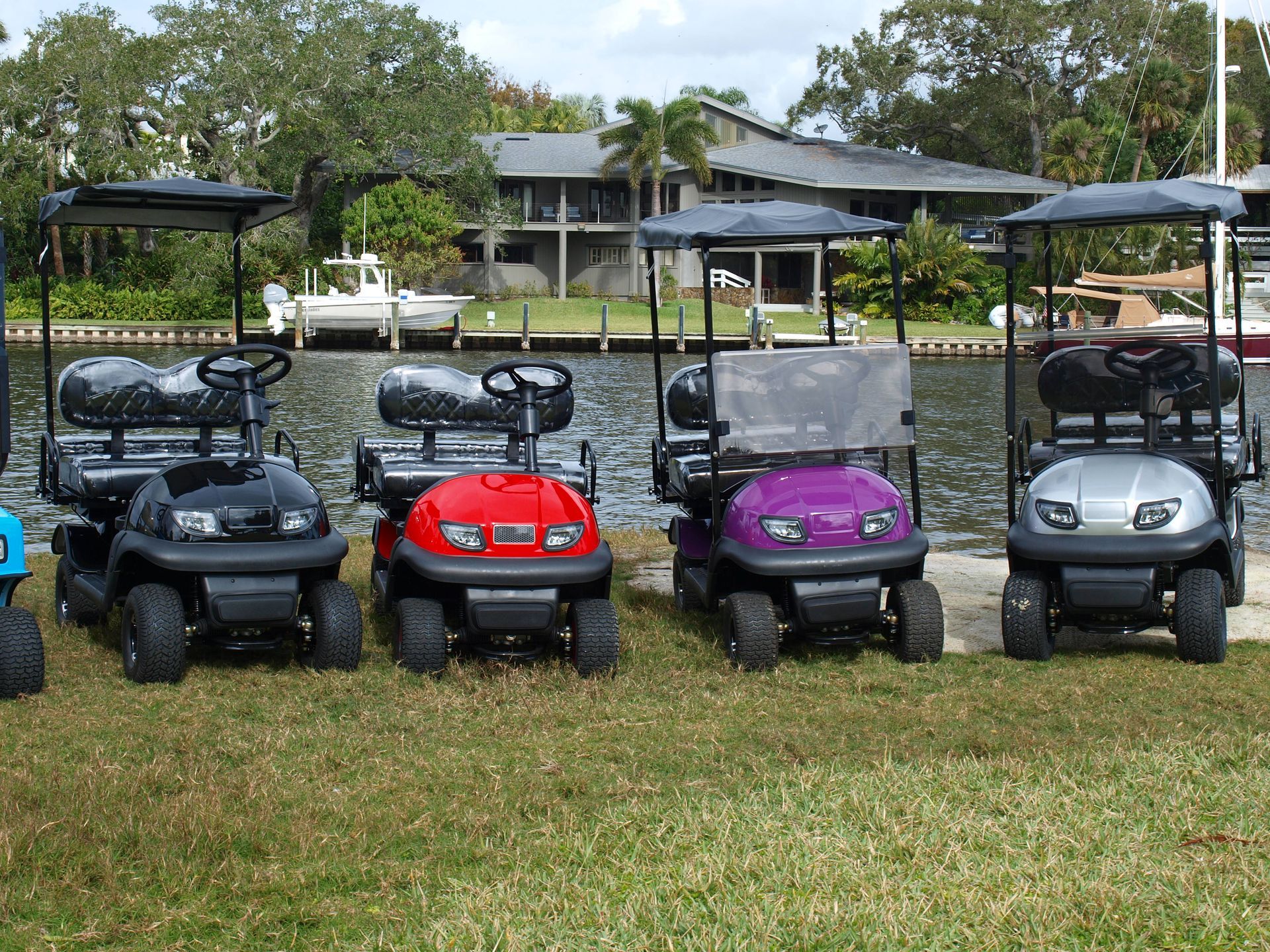 Four golf carts are parked in a grassy field in front of a body of water.