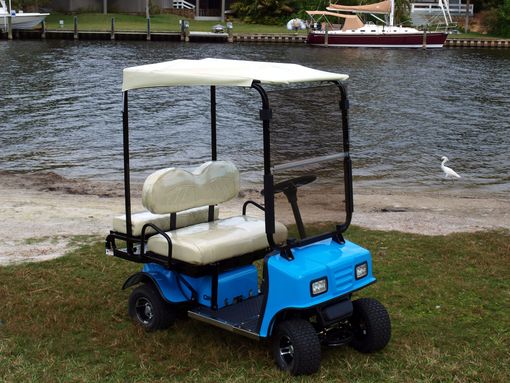 A blue golf cart is parked on the grass near the water