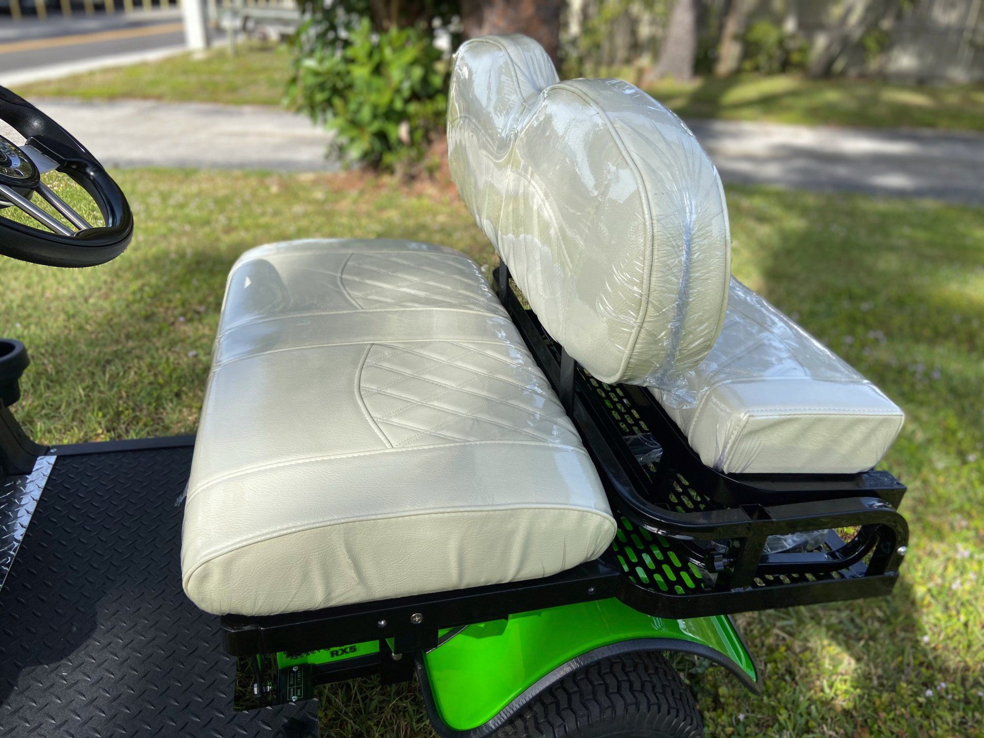 A green golf cart with white seats is parked in the grass.