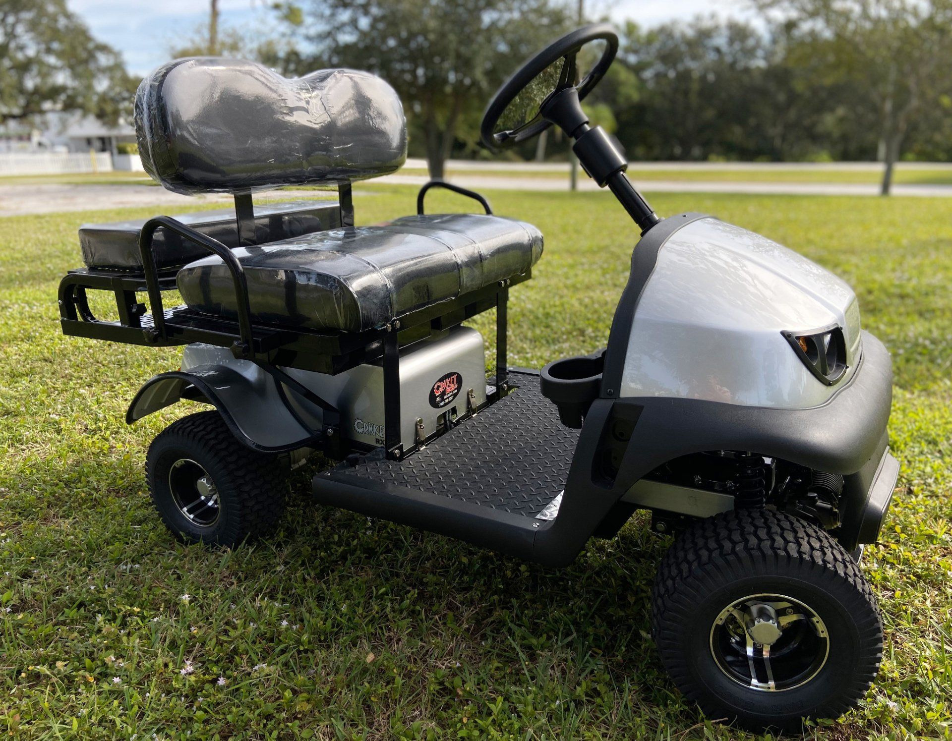 A silver golf cart is parked in the grass.