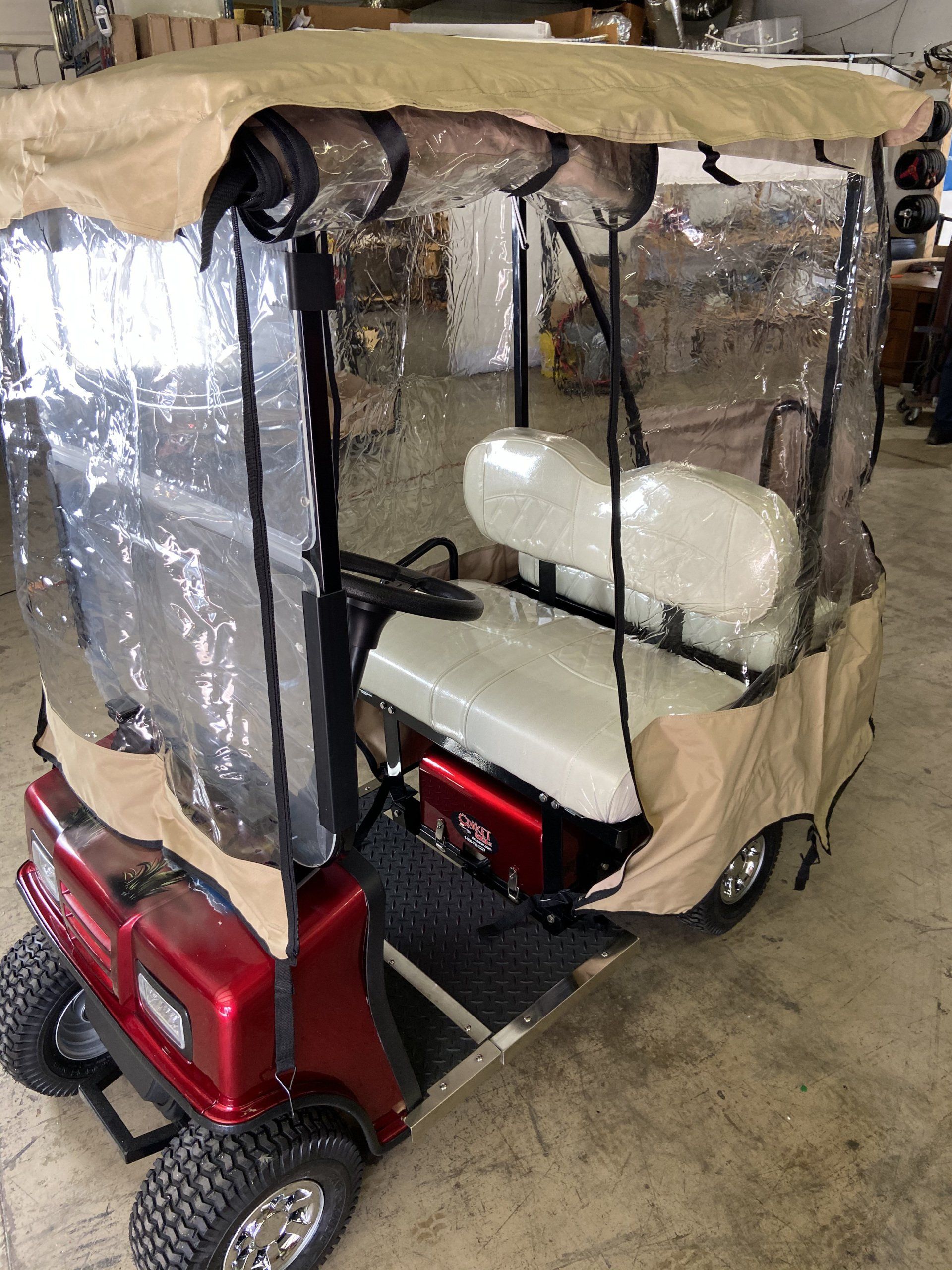 A red golf cart with a clear canopy is parked in a garage.