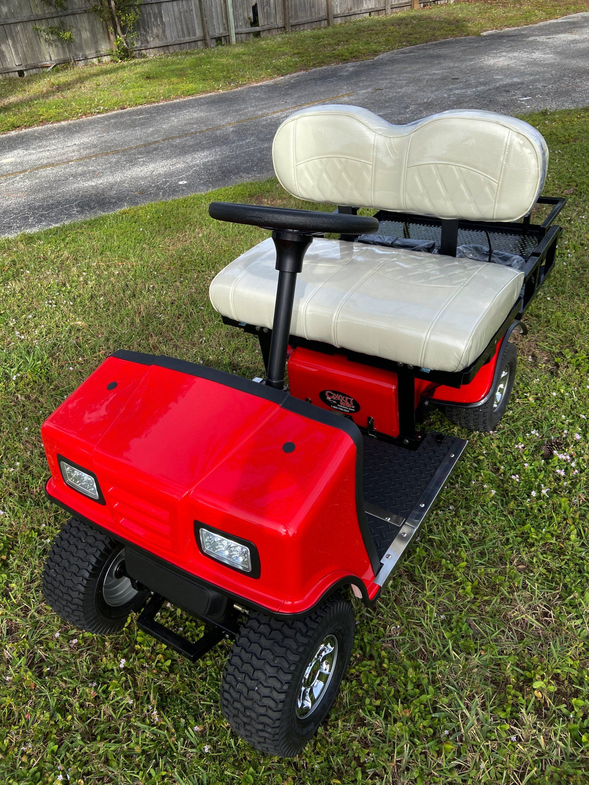 A red golf cart with white seats is parked in the grass.