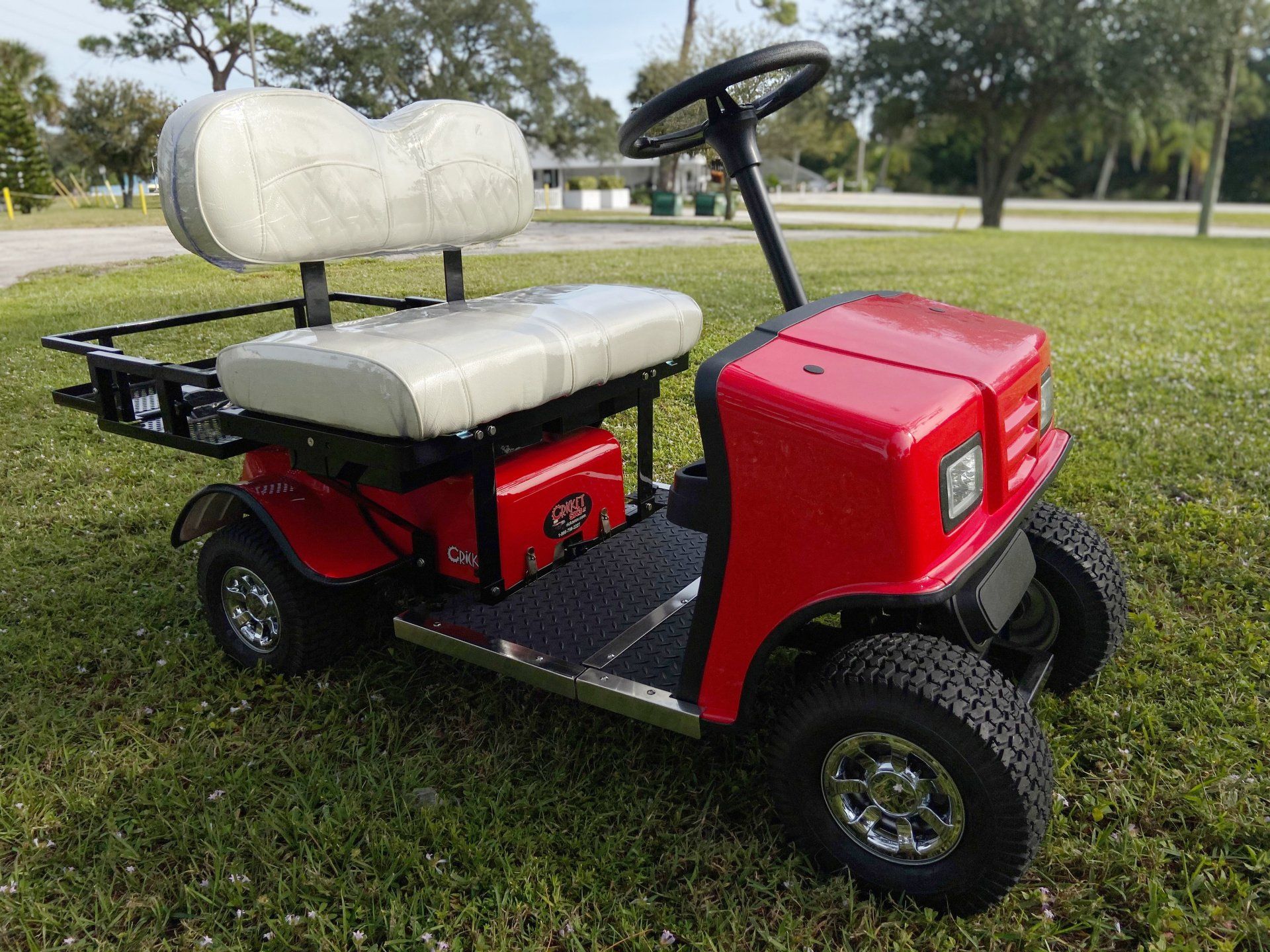 A red golf cart with a white seat is parked in the grass.