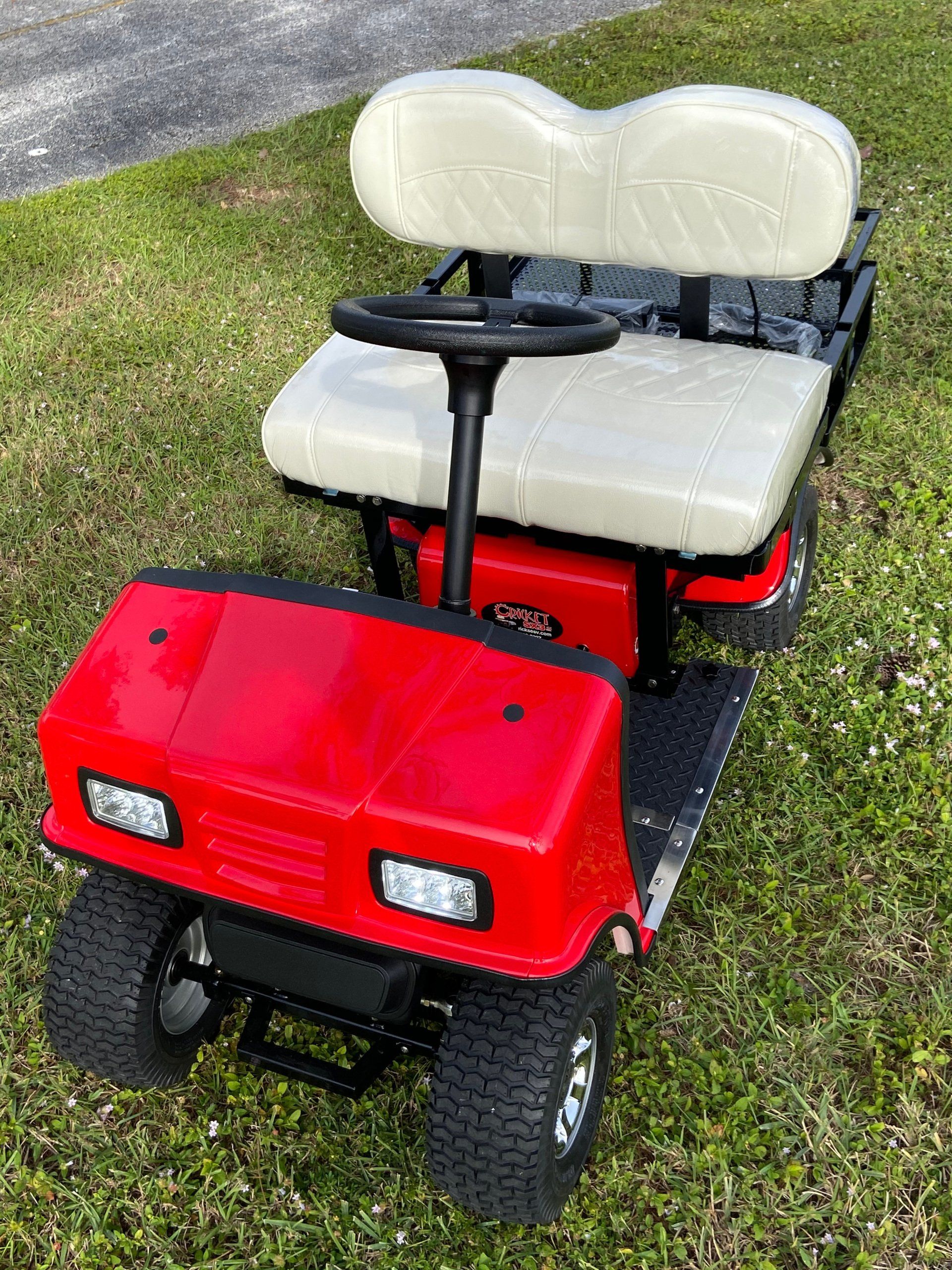 A red golf cart with white seats is parked in the grass.
