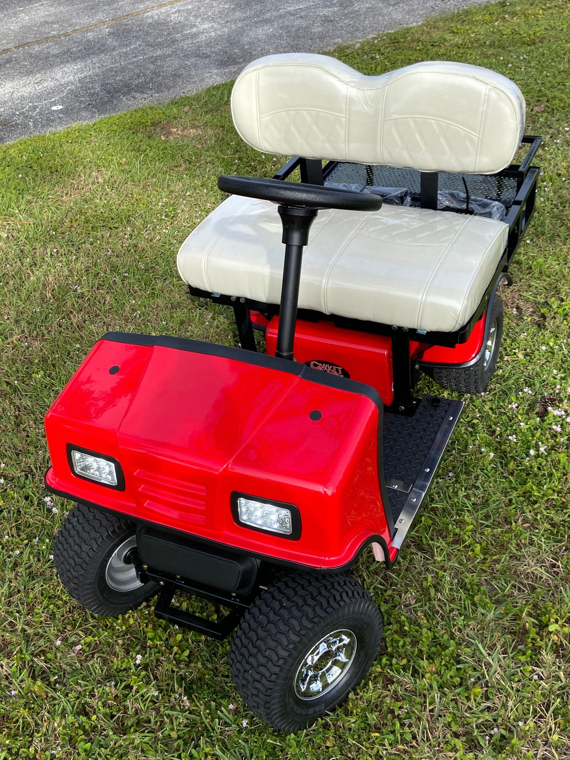 A red golf cart with white seats is parked in the grass.