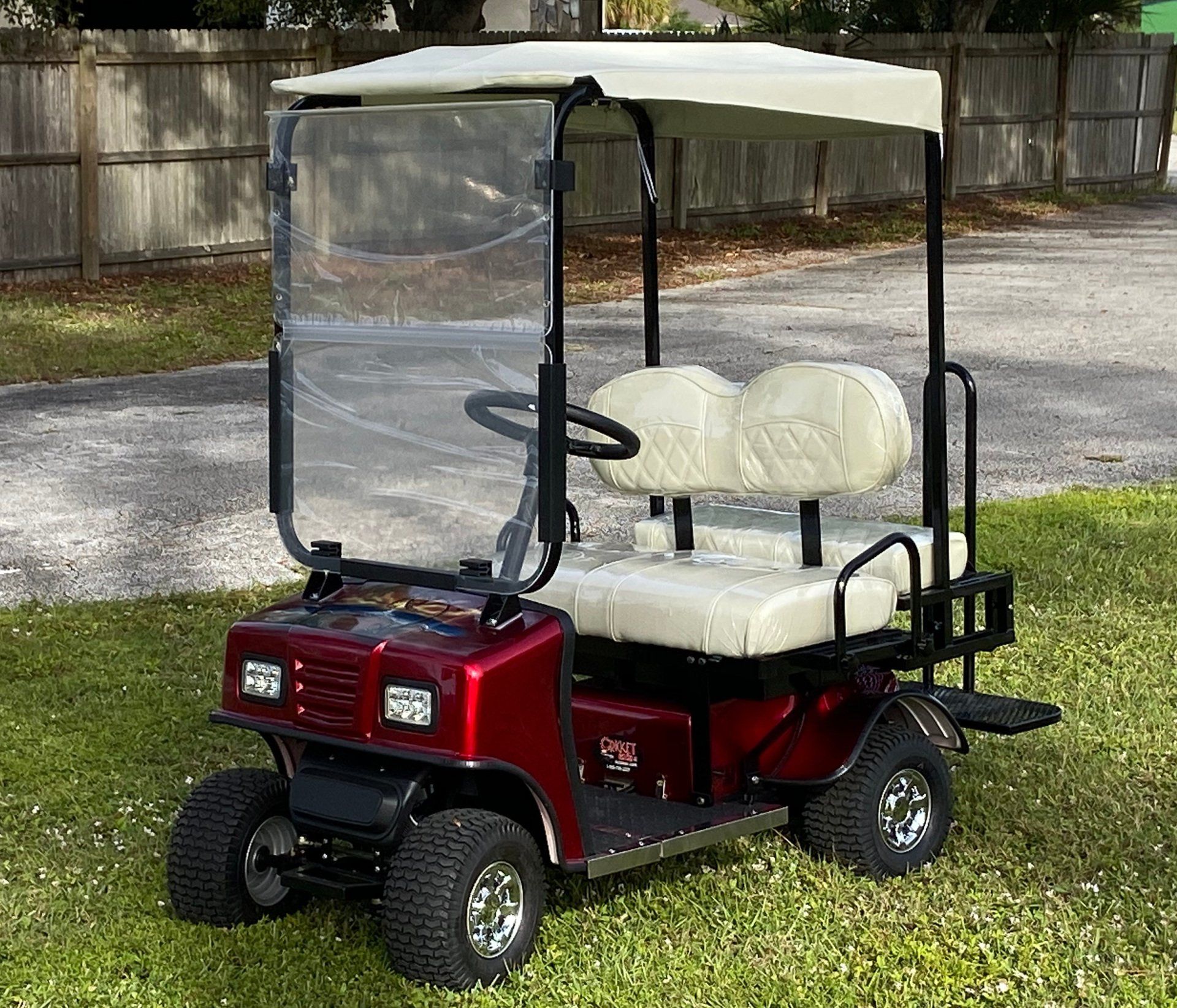 A red golf cart with white seats is parked in the grass.