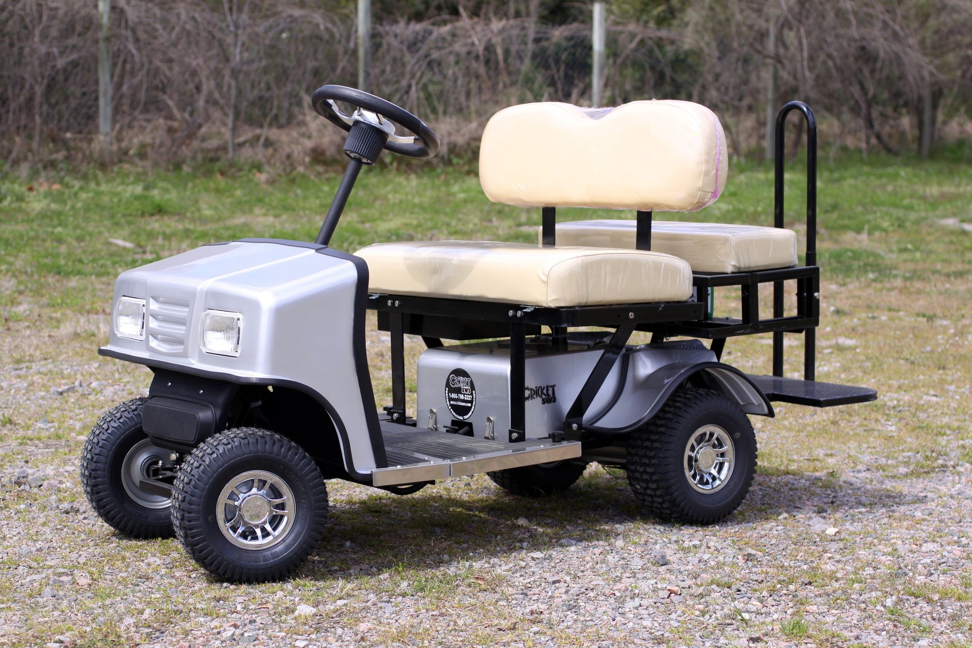 A silver golf cart with white seats is parked in a gravel lot.