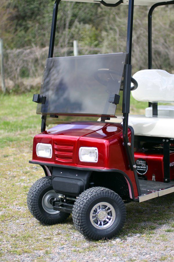 A red golf cart is parked in a gravel lot.