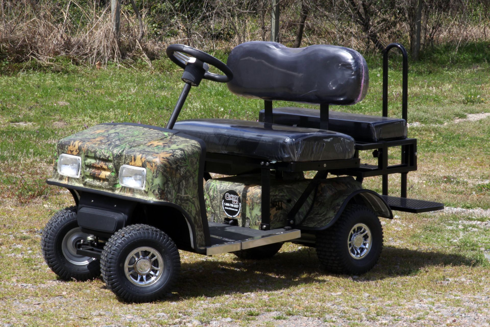 A camouflage golf cart is parked in the grass.