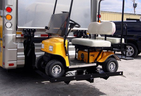 A yellow golf cart is attached to the back of a bus