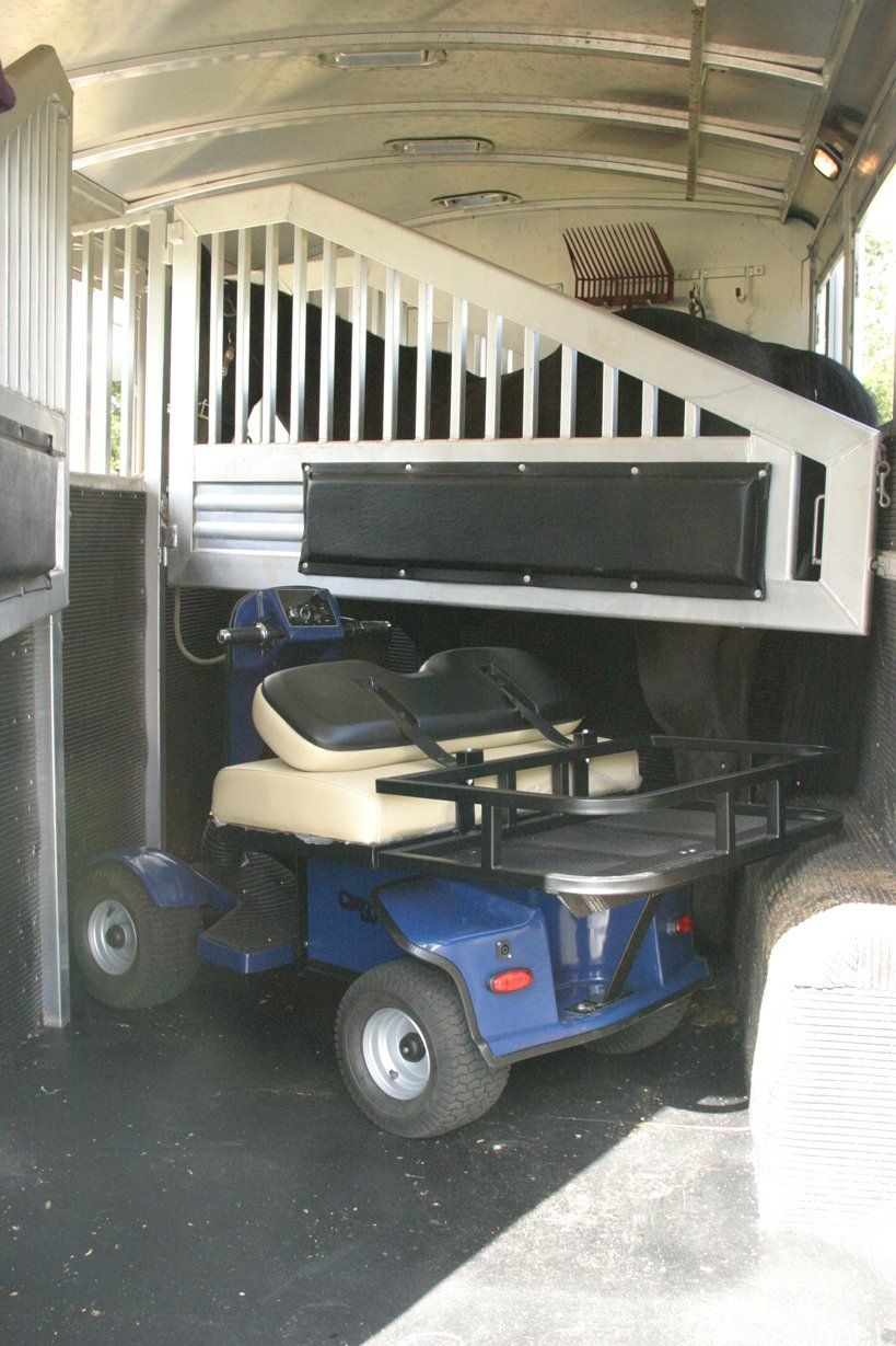 A blue golf cart is parked in the back of a horse trailer