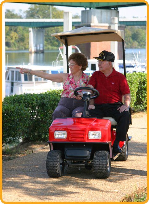 A man and a woman are riding a red golf cart.