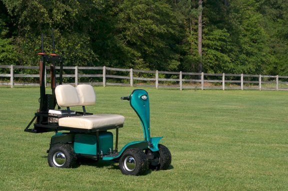 A green golf cart is parked in a grassy field.