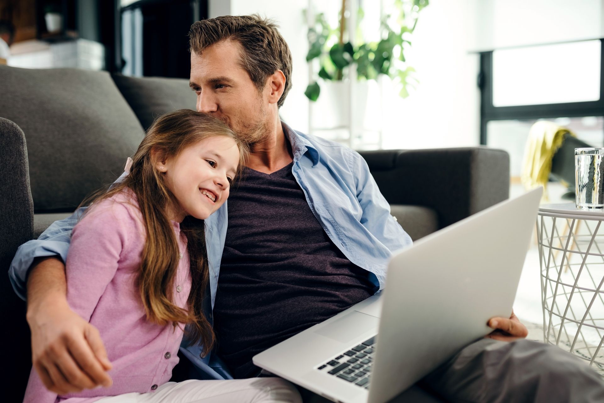 Man kisses girl's head as they sit together using a laptop in a living room.