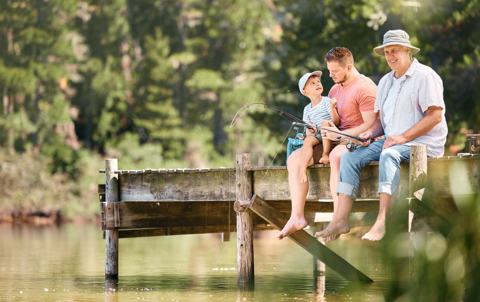 Three people fishing from a wooden dock at a lake.