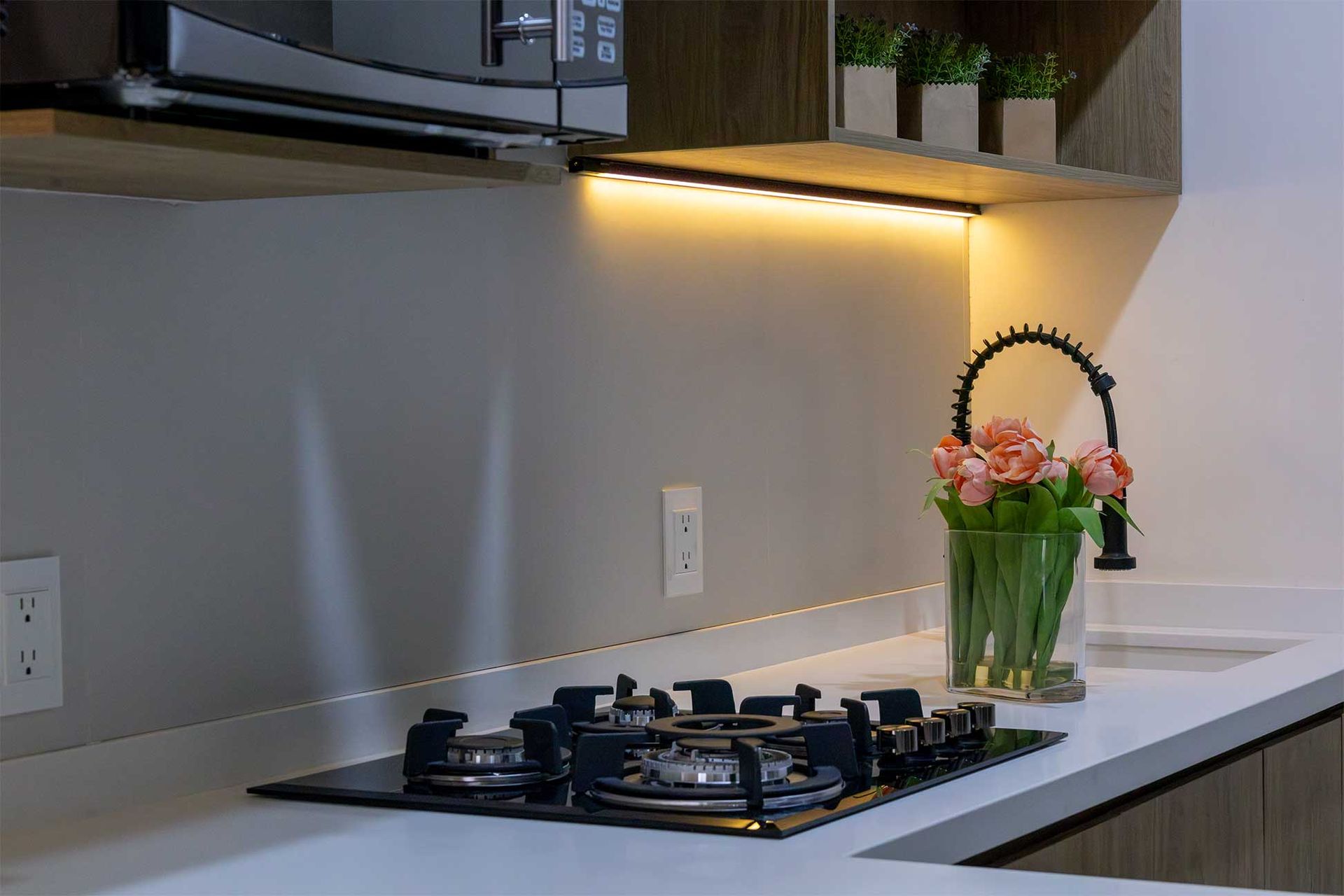Una cocina con estufa, fregadero, microondas y un jarrón de flores.