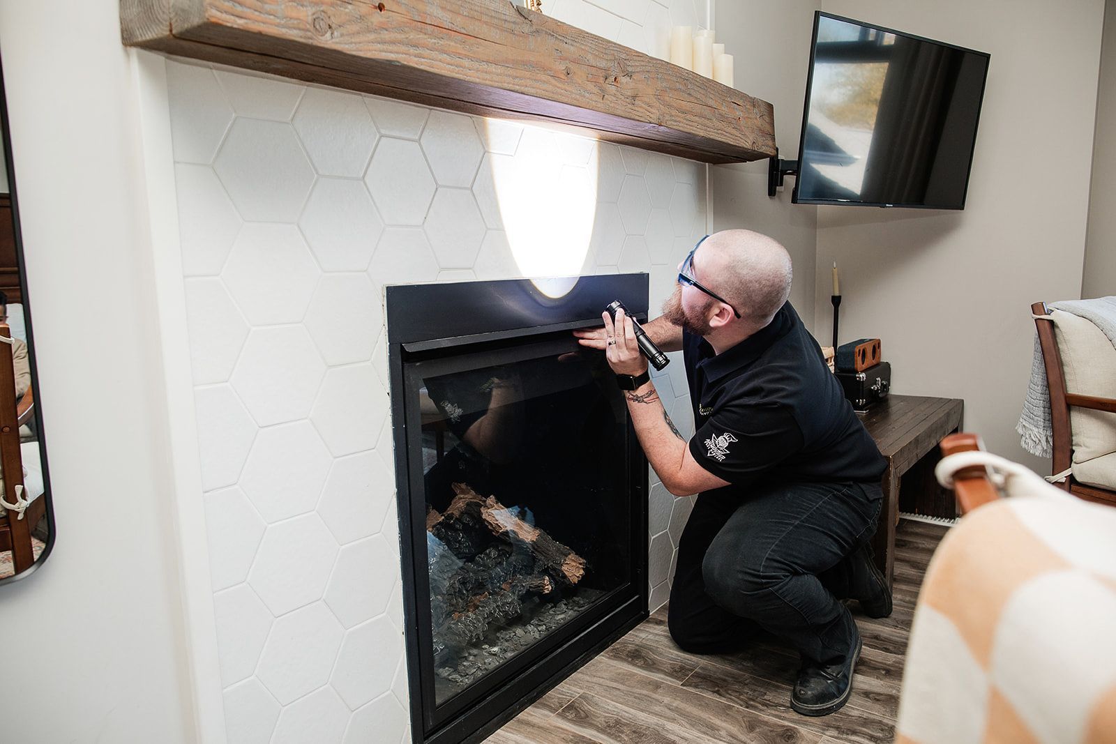 Person kneeling beside a black fireplace, adjusting a tool near the hearth in a cozy living room.