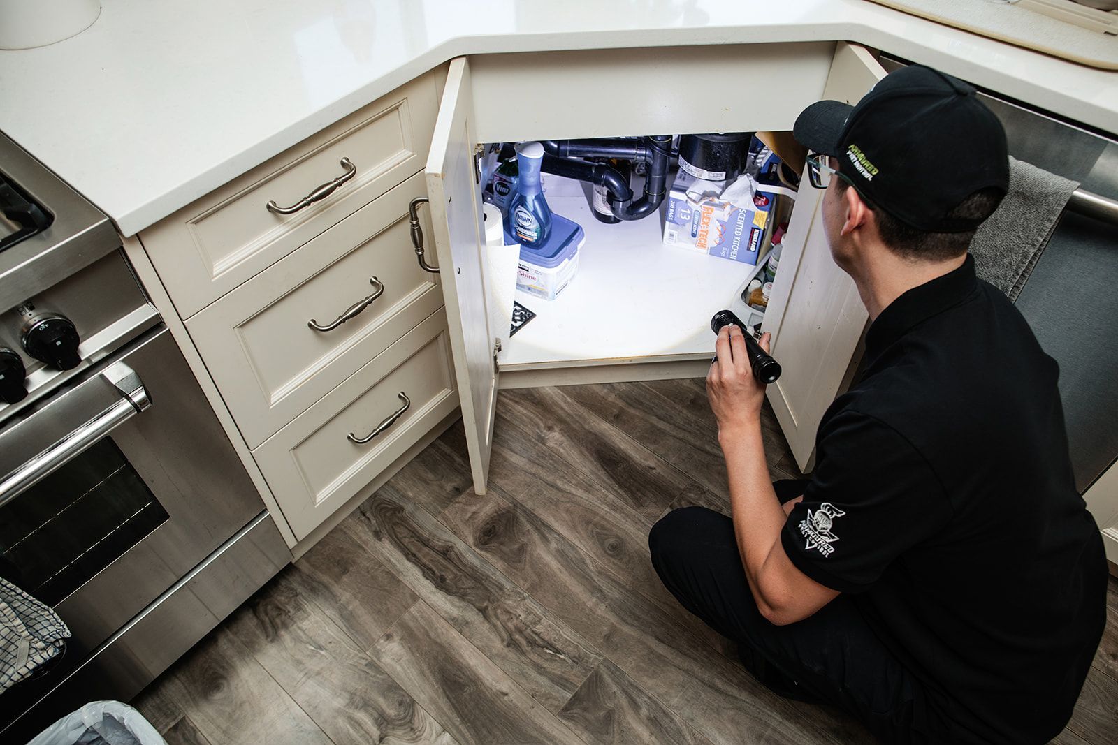 Technician inspecting under-kitchen-cabinet wiring with a flashlight in a kitchen floor cabinet opening