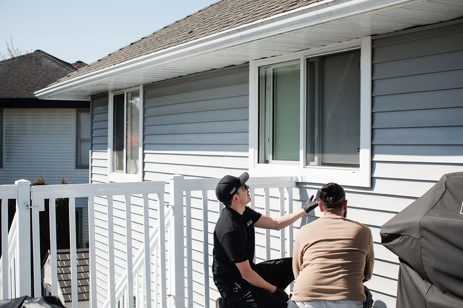 Two people talking on a porch outside a white house with siding and a garage door.