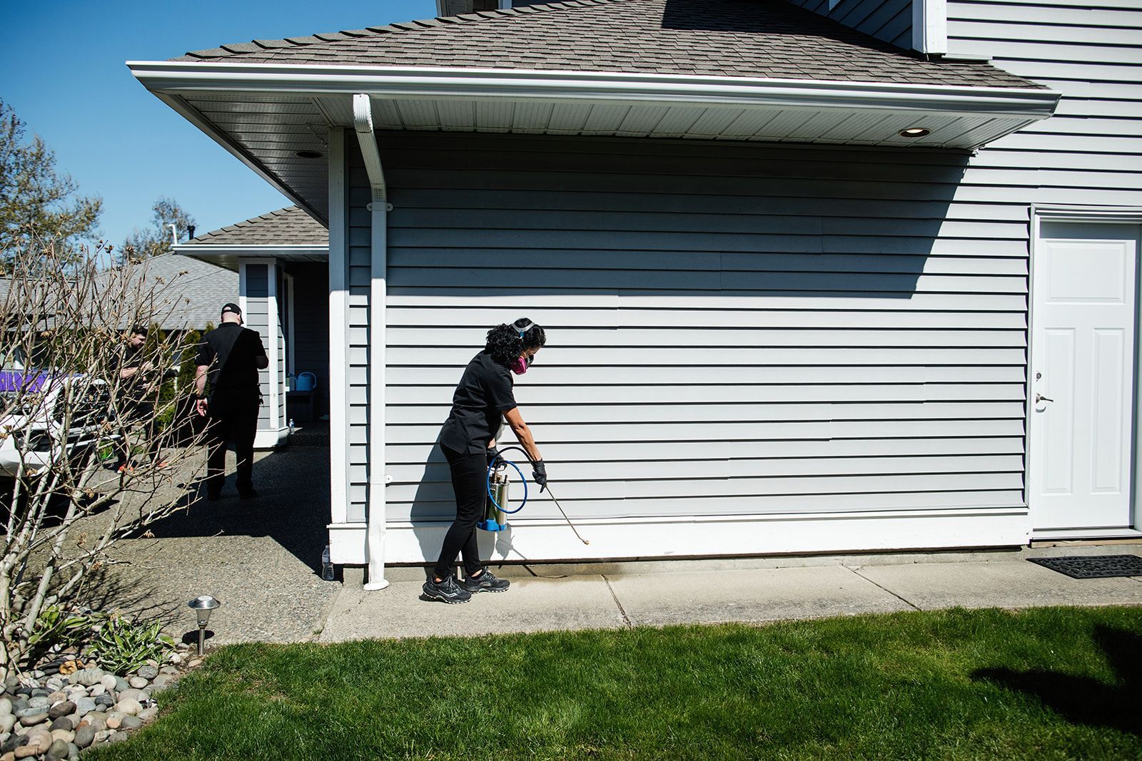 Person using a walker beside a house with another person in the background and a white door nearby