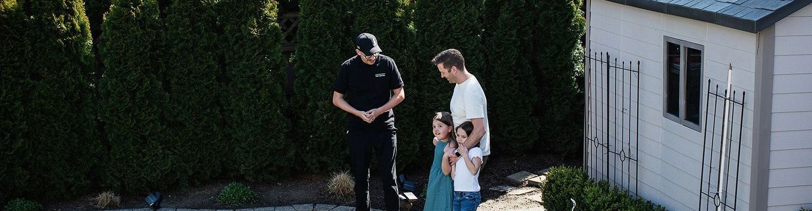 A man and two children are standing next to a police officer in front of a shed.