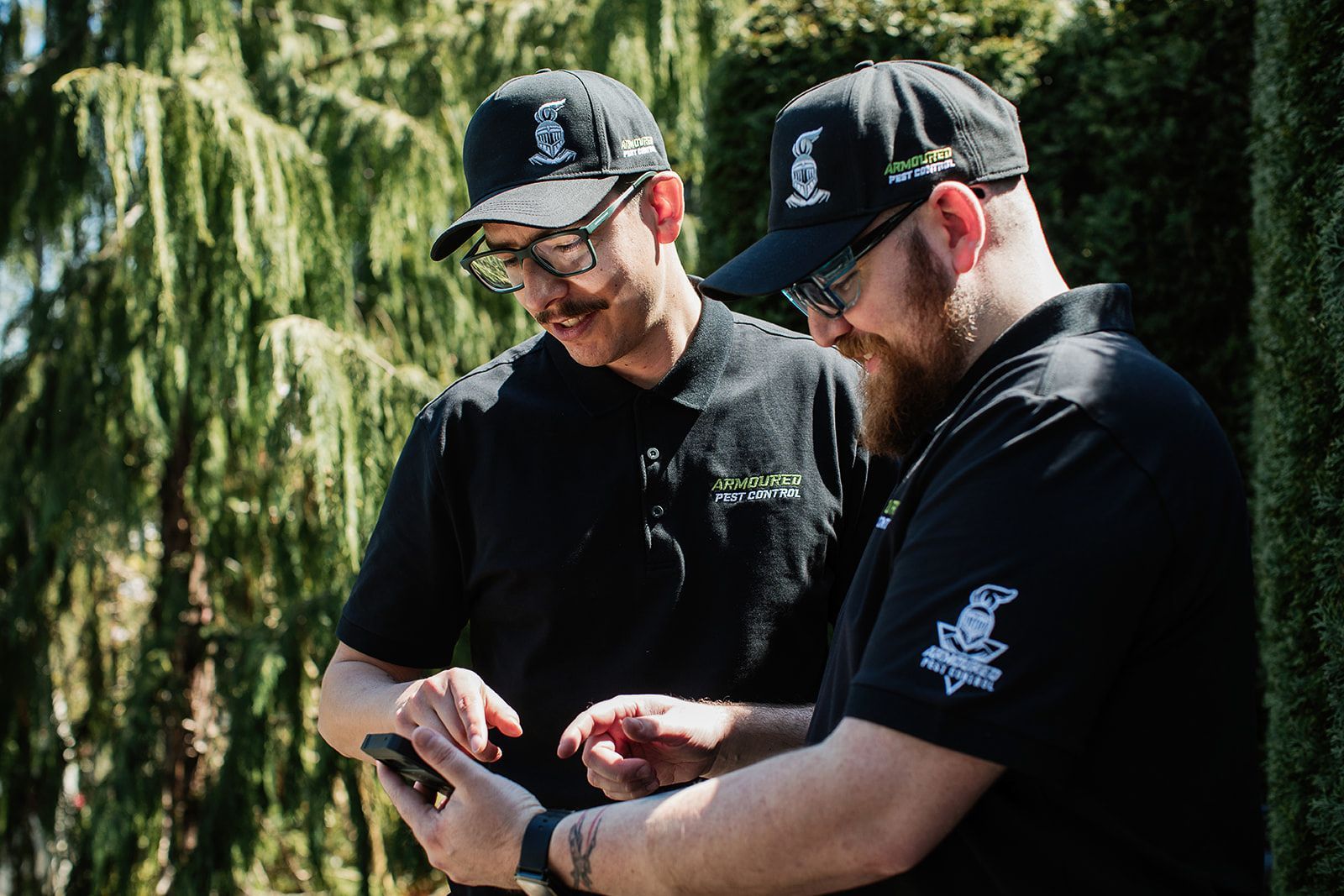 Two men in black shirts and hats looking at a phone outdoors.