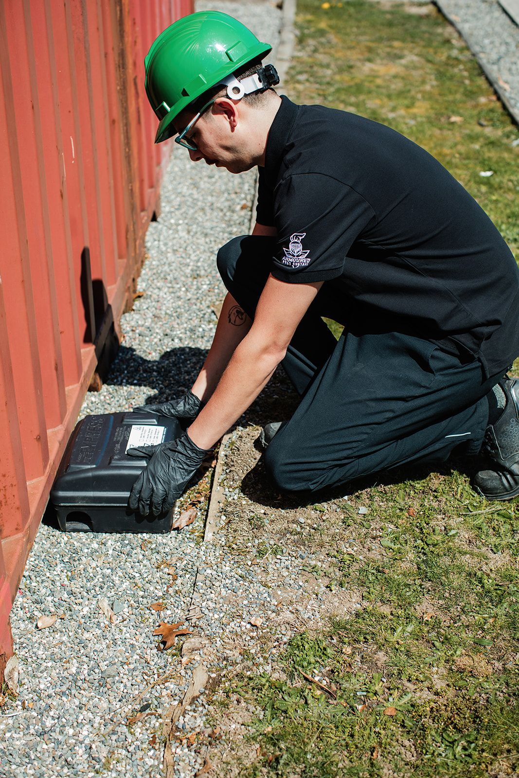 A closed black mouse trap with a red handle, placed on a tile floor near a wall.