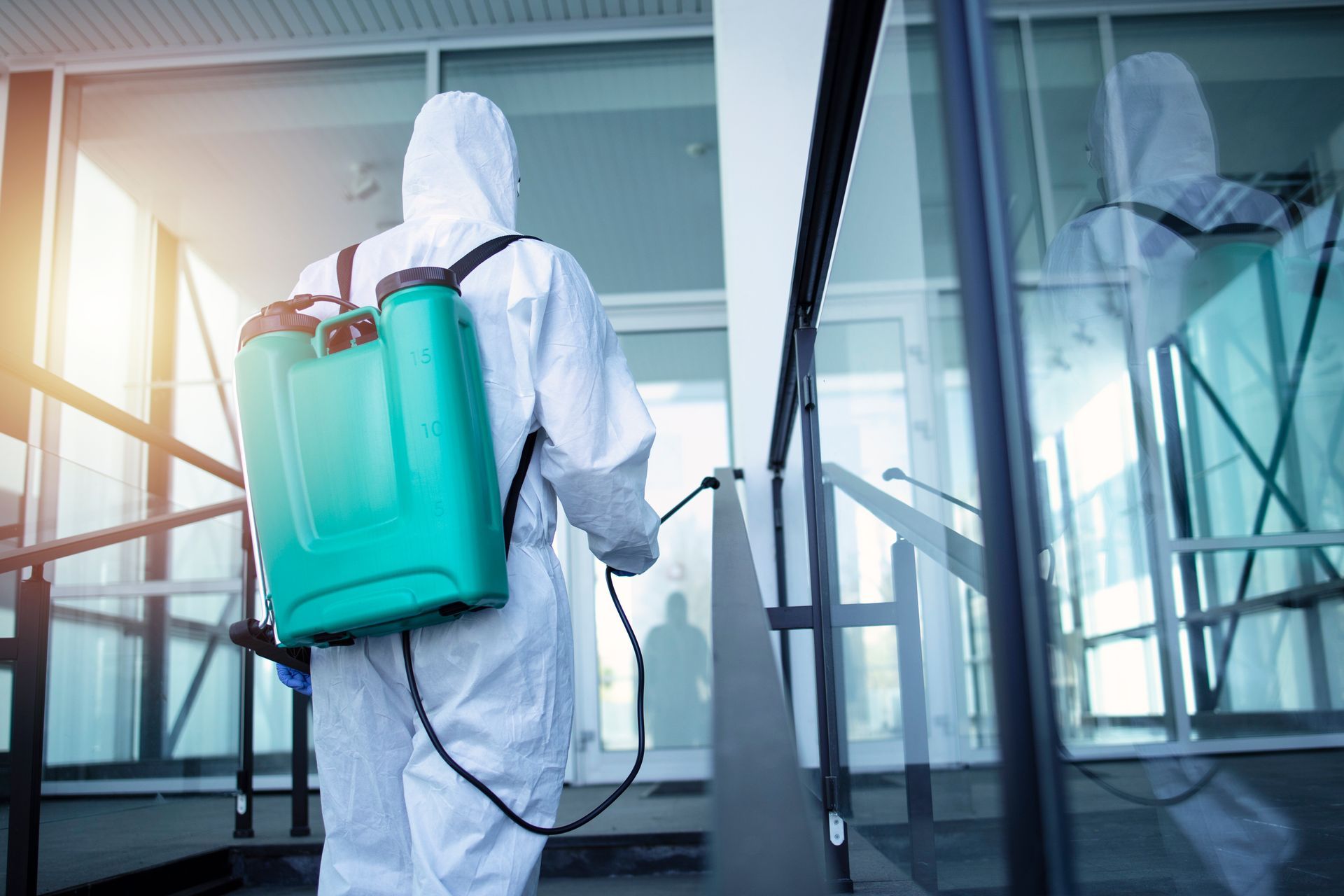 A man in a protective suit is disinfecting a building with a sprayer.