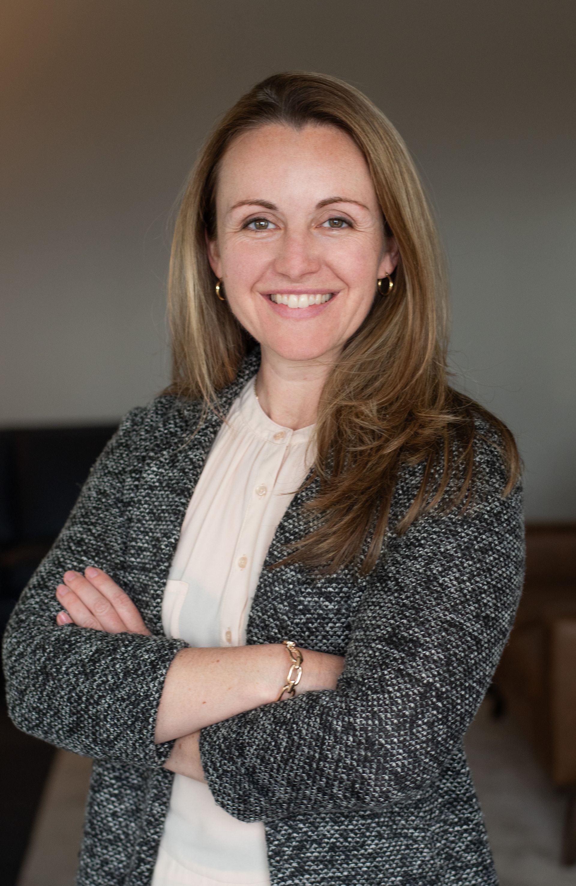 Woman in a light suit smiles, leaning on a railing inside a modern building with high ceilings.