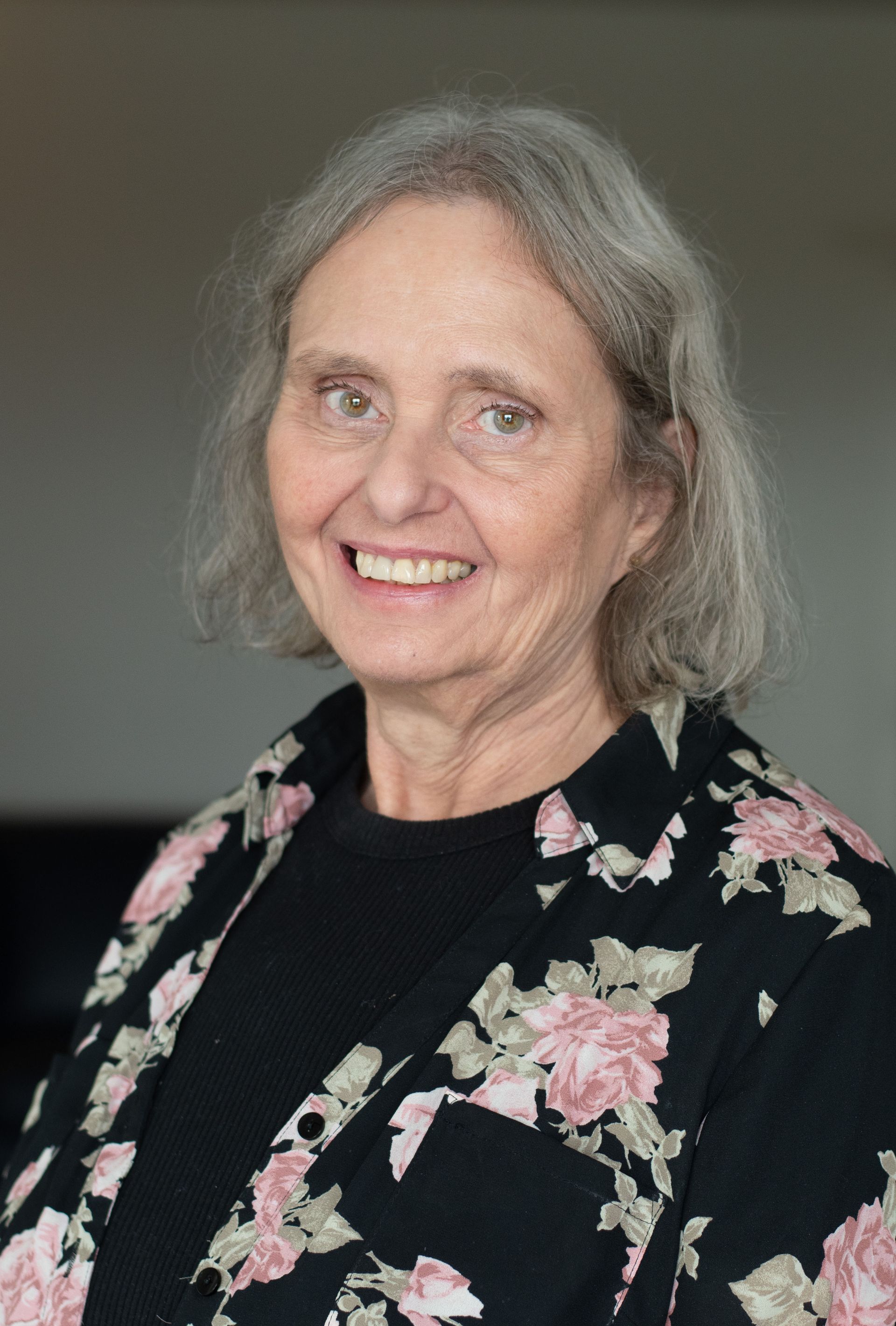 Woman in a light suit smiles, leaning on a railing inside a modern building with high ceilings.