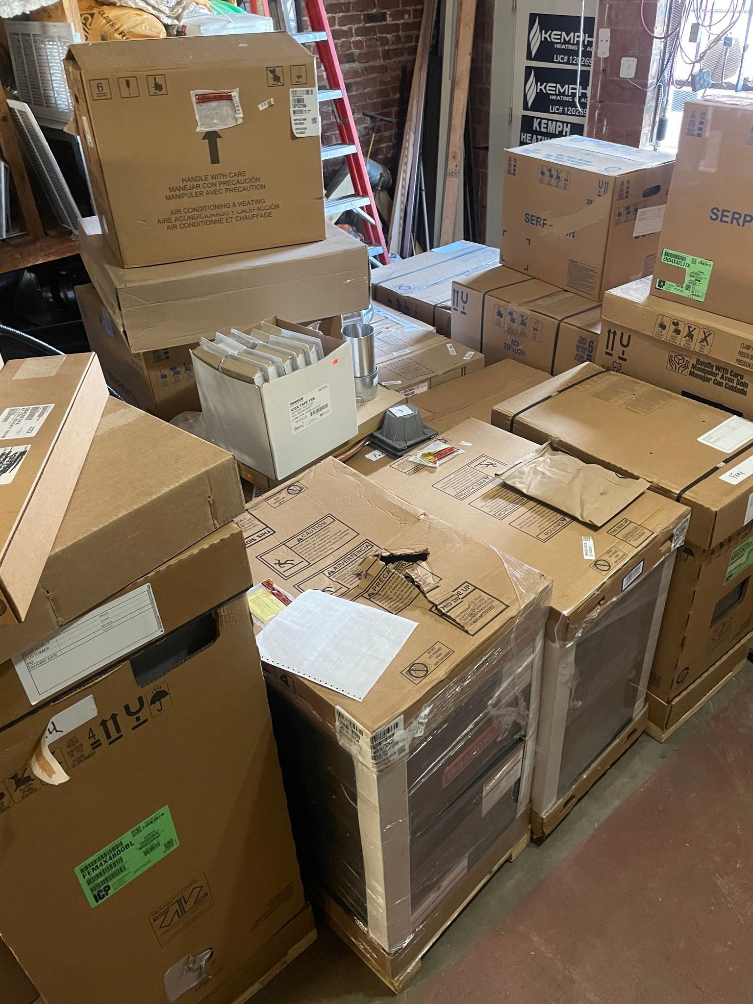 Boxes stacked in a room, likely a warehouse or storage area. Some boxes on a pallet, and other boxes piled higher.