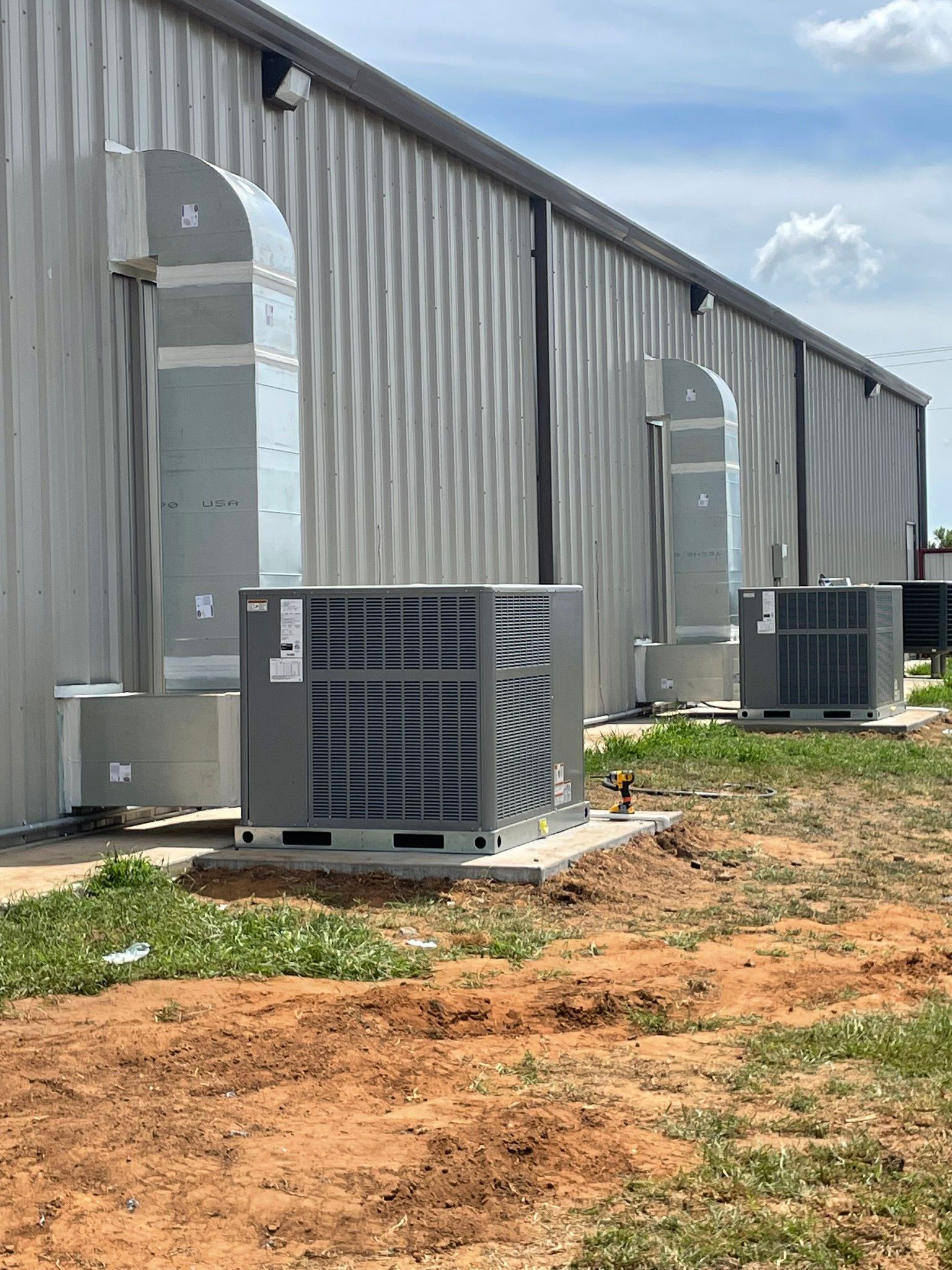 Three HVAC units along a metal building, with ductwork extending upward.
