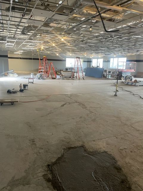 Construction site interior: unfinished concrete floor, ladders, exposed ceiling, walls being built.