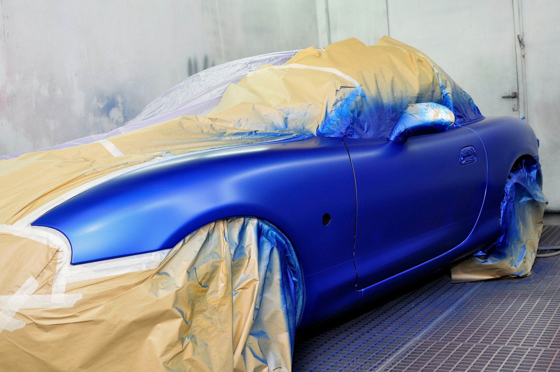 Un'auto sportiva blu viene verniciata in una cabina di verniciatura