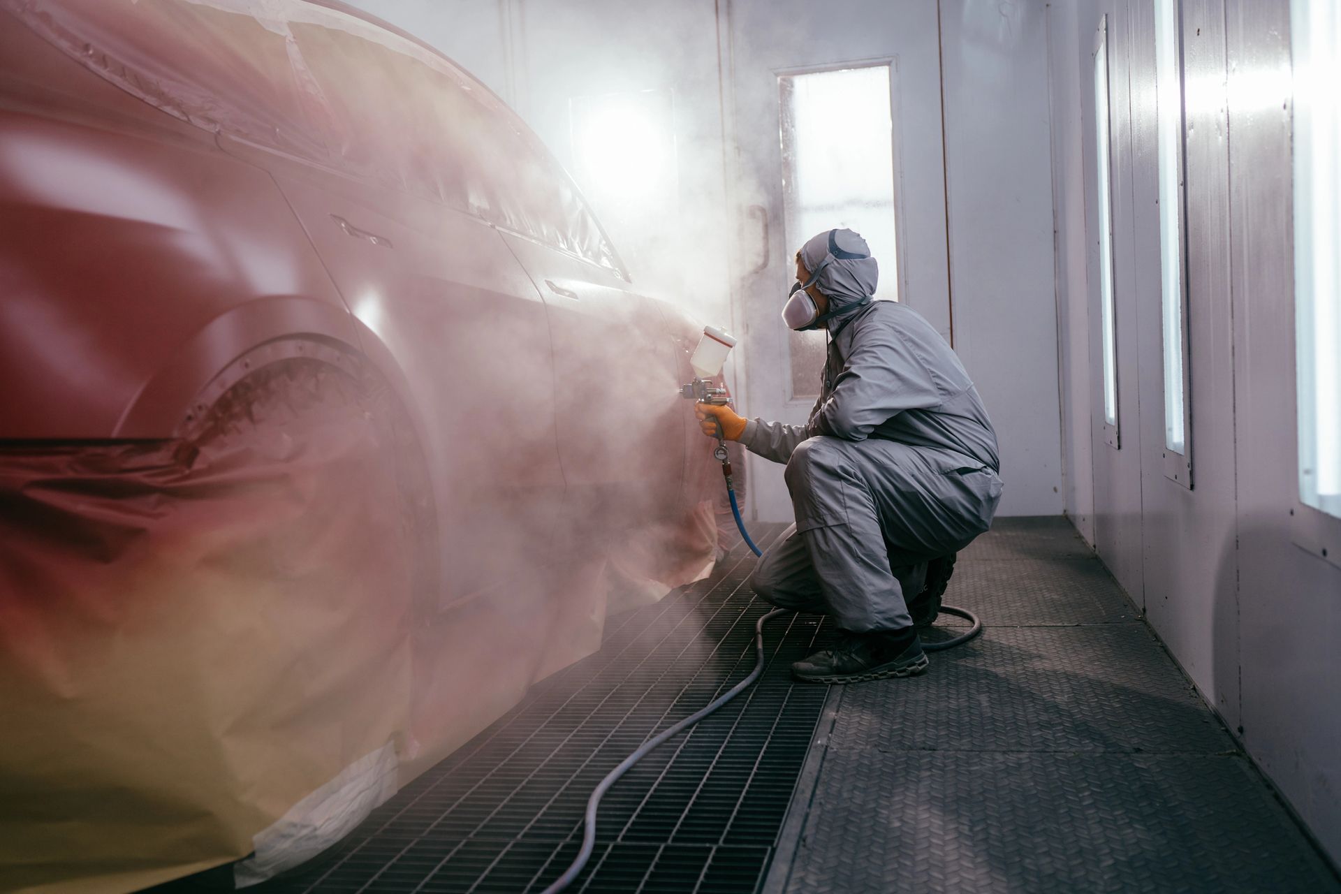 Persona con tuta protettiva che vernicia un'auto