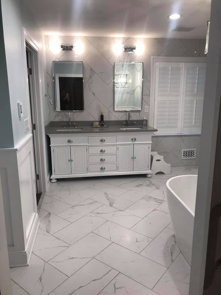 White marble bathroom with double vanity, mirrors, and a freestanding tub.