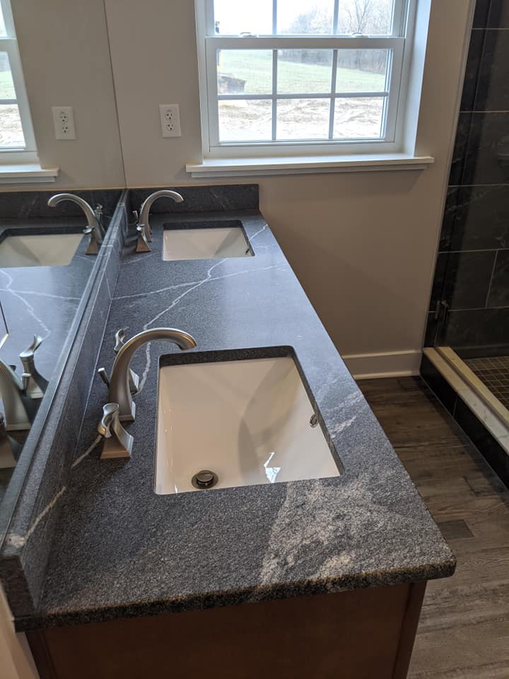 Bathroom vanity with two sinks and a dark gray countertop, next to a window.