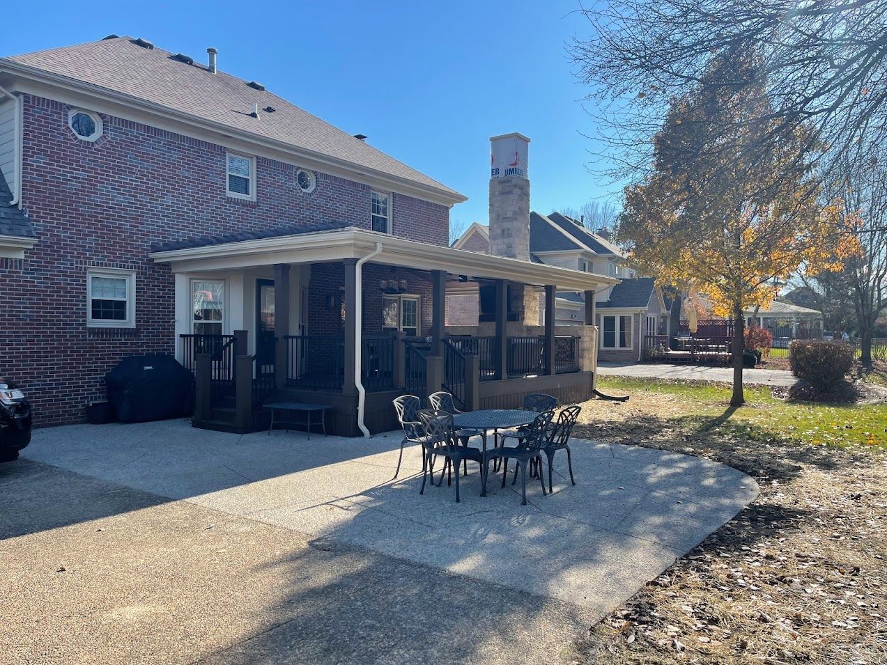 Brick house with covered patio, outdoor table and chairs, paved area, and blue sky.