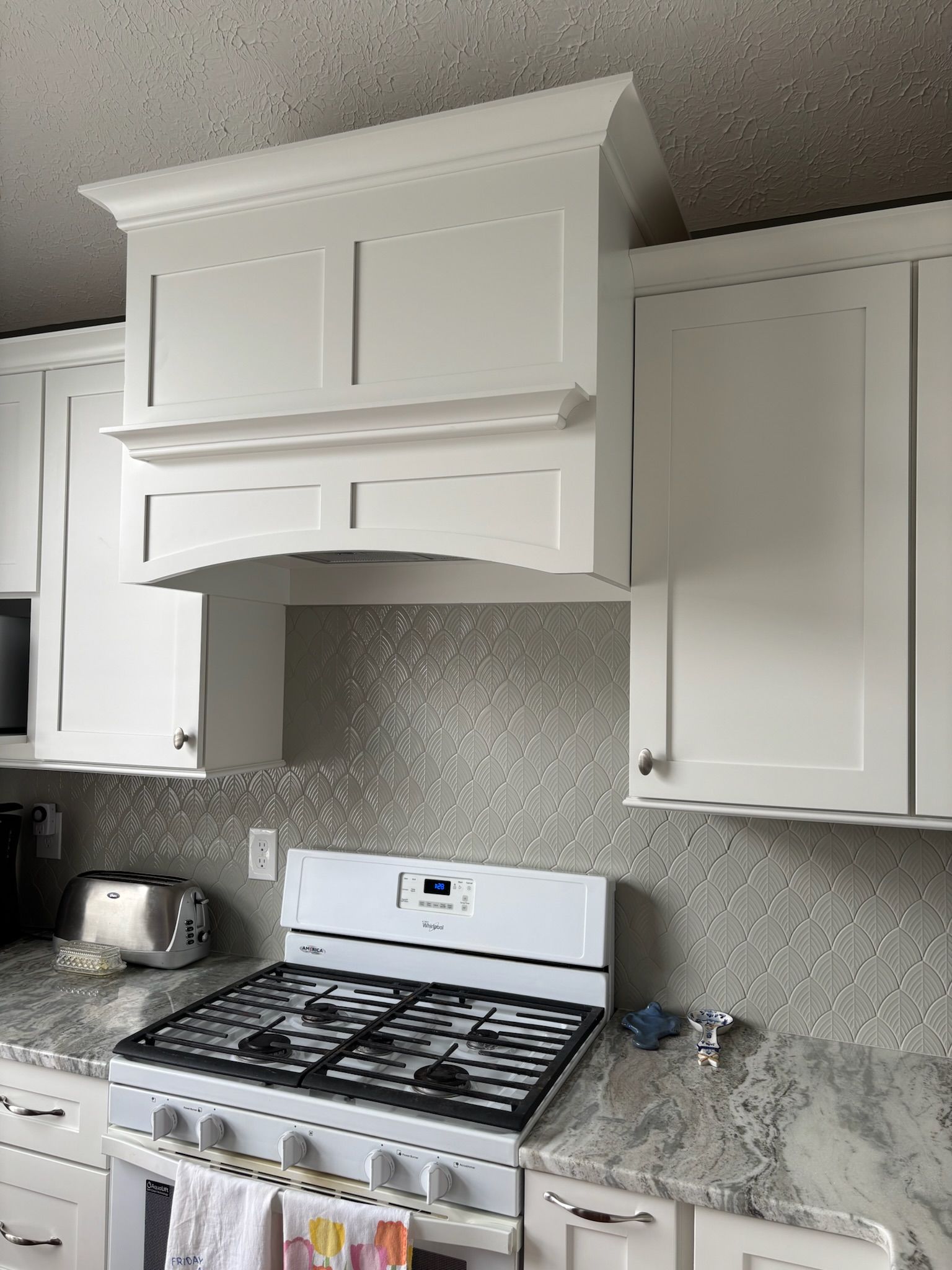 White kitchen with stove, range hood, and cabinets against a shimmering backsplash.
