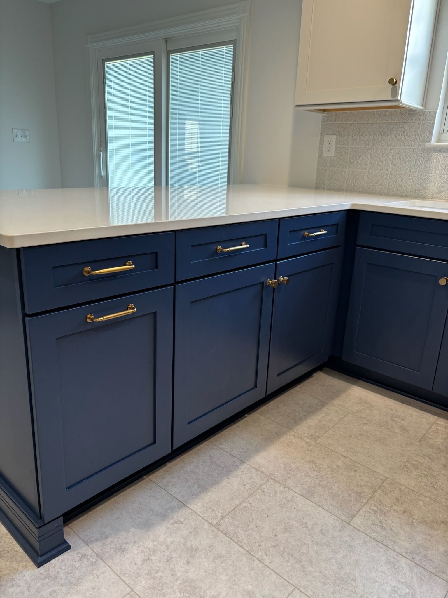 Blue kitchen cabinets with gold handles and white countertop.
