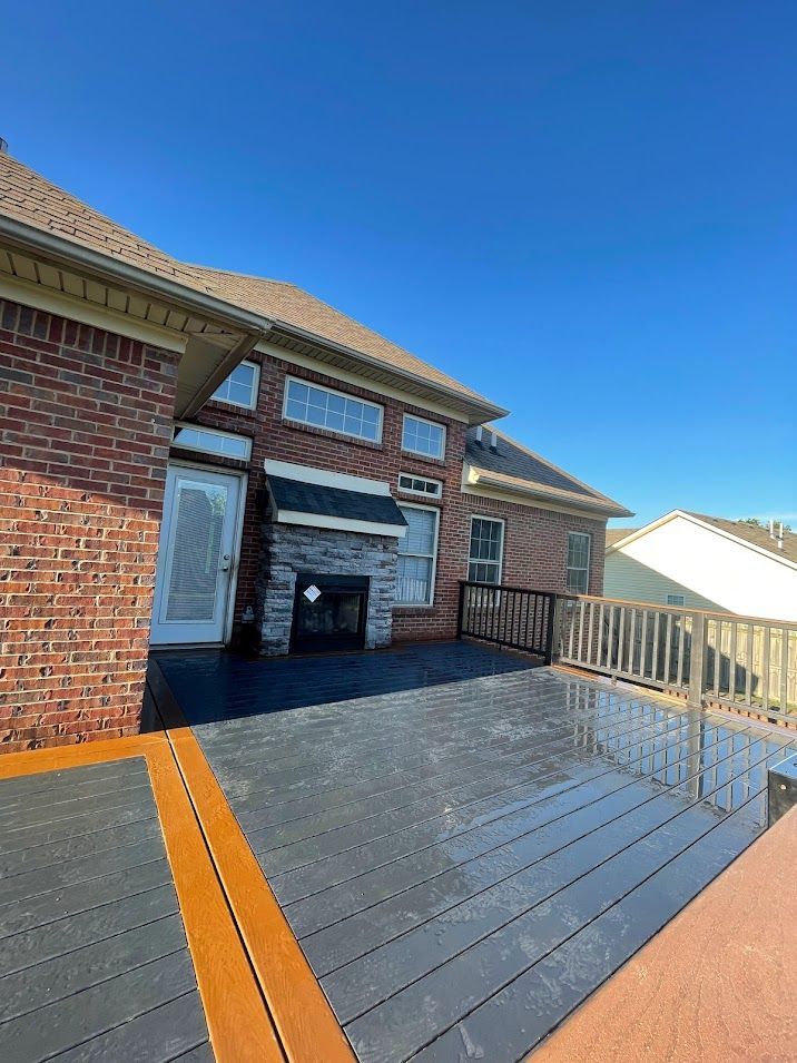 Backyard deck with brick house, fireplace, blue sky.
